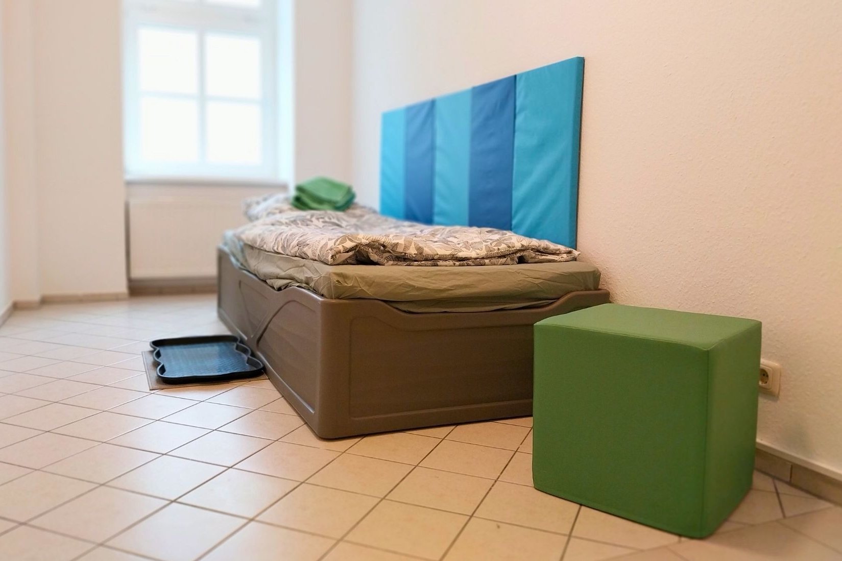 Dieses Foto zeigt ein weiteres Einzelzimmer mit Bett, Sitzhocker und großem Fenster.