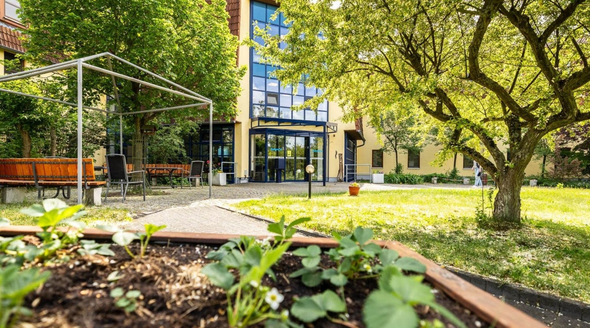 Das Bild zeigt den Eingangsbereich des Altenpflegeheims "Friedenshöhe" in Radeburg mit viel Wiese und Bäumen drumherum.