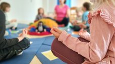 Dieses Bild zeigt einen Ausschnitt von Kindern, die beim Yoga im Schneidersitz im Kreis sitzen. Auch die Yohalehrerin, eine pädagogische Fachkraft in der Kita Eckstein, ist zu erkennen.
