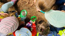Eine Gruppe von Kindern beochtet mit Lupen Insekten auf dem Waldboden.