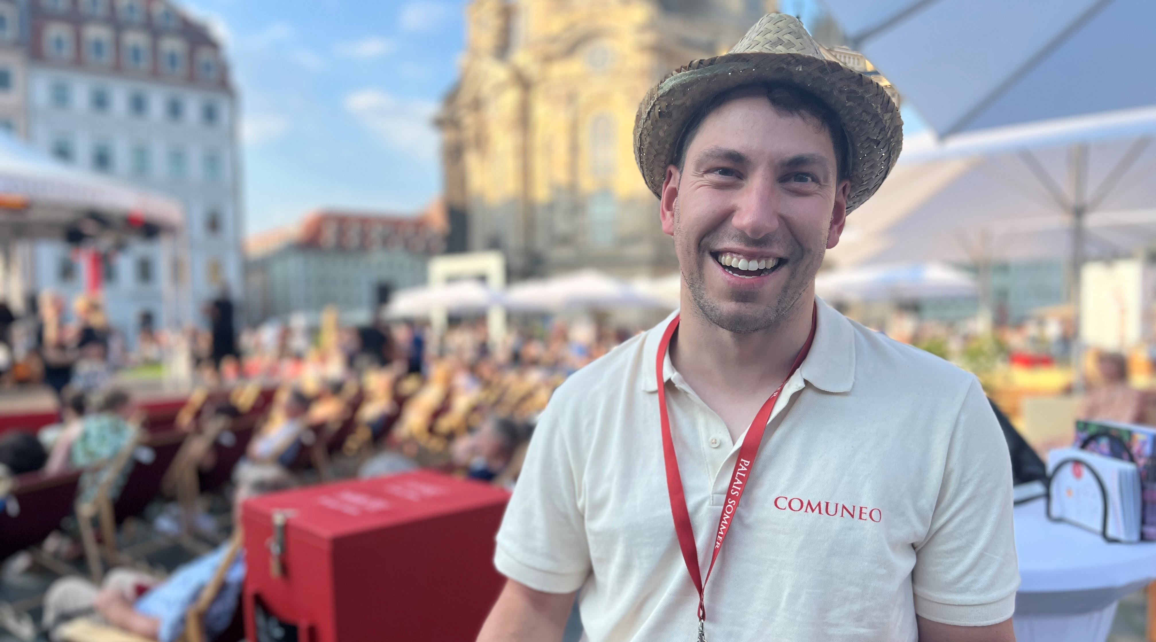 Ein Beschäftigter der Wichern-Werkstätten lächelt in die Kamera. Im Hintergrund sieht man das Publikum des Palais Sommer Festivals und die Frauenkirche. 