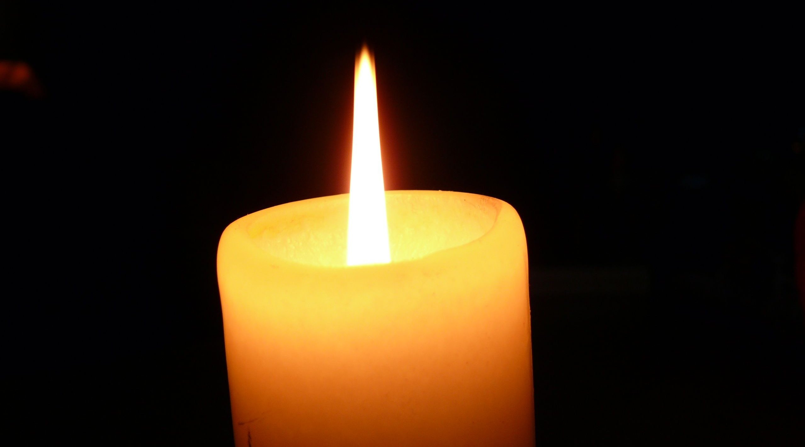Das Bild zeigt eine brennenden Kerze vor schwarzem Hintergrund.