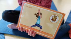 Auf diesem Bild hält ein Kind eine Karte mit eine Yoga-Übung, dem Helden, in die Kamera.