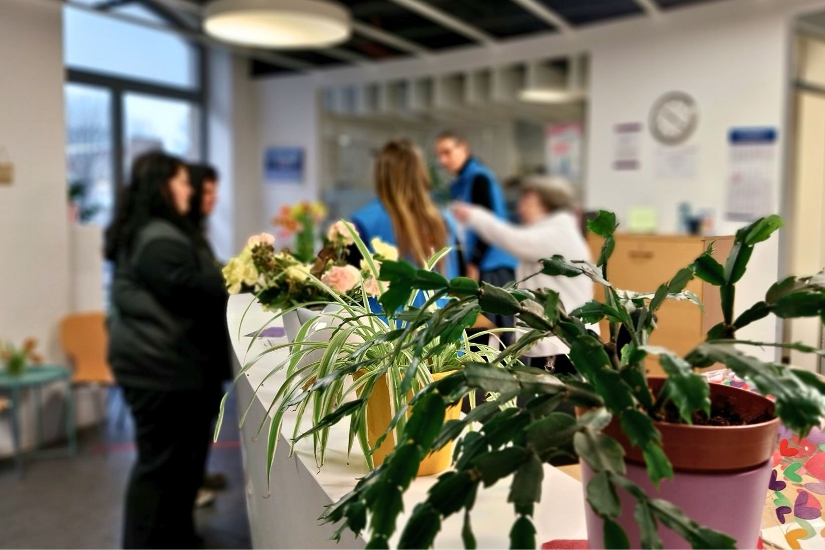 Das Bild zeigt den Innenraum der Bahnhofsmission Dresden. Haupt- und ehrenmtliche Mitarbeiterinnen stehen hinter dem Empfangsdresden und kümmern sich um zwei Gäste.