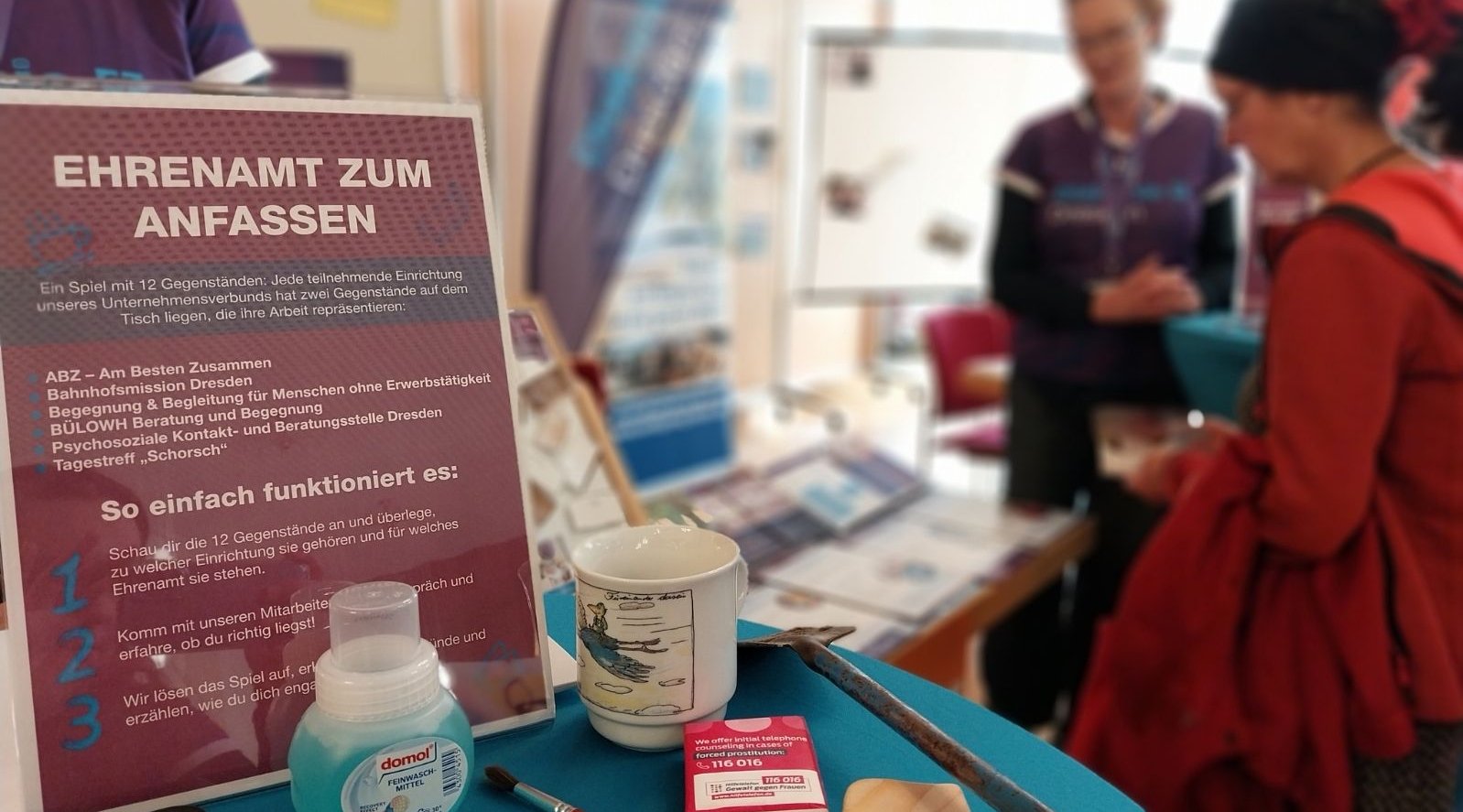 Das Bild zeigt einen Ausschnitt eines Infostandes der Diakonie Dresden. Im Hintergrund sind Menschen zuerkennen. 
