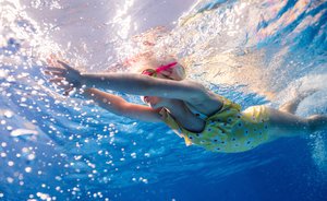 Dieses Foto ist im Wasser aufgenommen und zeigt ein Mädchen in gelbem Badeanzug und mit pinker Schwimmbrille beim Brustschwimmen.