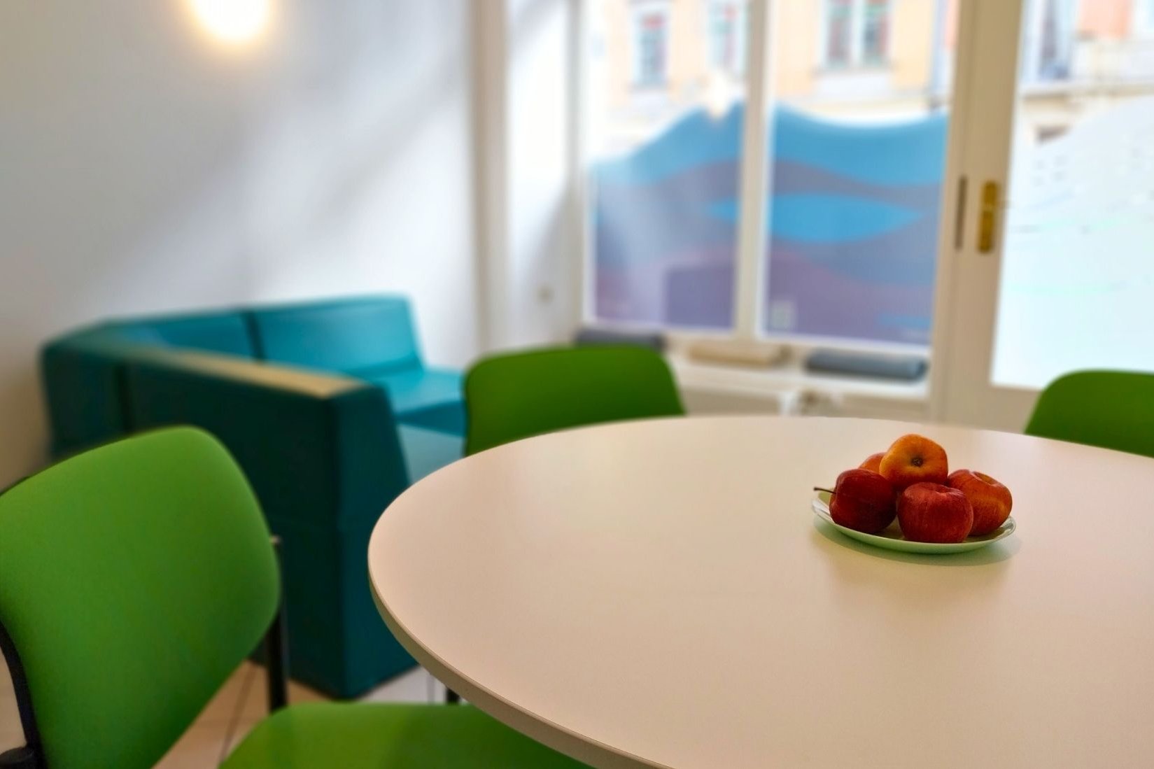 Dieses Bild zeigt den Gemeinschaftsbereich der Koje mit Blick zur Fensterfront zur Straße. Der Tisch mit Stühlen sowie die Sofaecke sind zu erkennen.