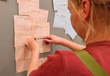 Dieses Foto zeigt eine Frau, die einen Zettel an einer Pinnwand anbringt. Auf den Zetteln konnten die Gäste schreiben, was Telefonseelsorge für sie bedeutet. Auf einem Zettel wurde zum Beispiel "Erdung" geschrieben.