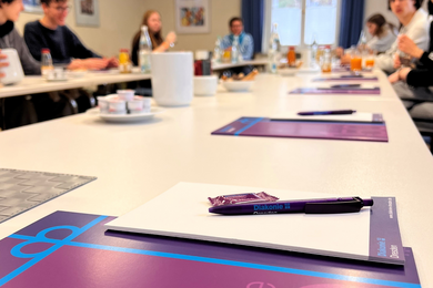 Das Bild zeigt Tische in einem der Tagungsräume der Diakonie Dresden. Schulerinnen und Schüler sitzen an den Tischen. Auf den Tischen befinden sich Prospekte und Kugelschreiber.   