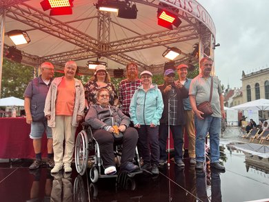 Das Bild zeigt eine Gruppe Menschen auf der Bühne des Palais-Sommer-Festivals. Sie tragen Headset-Mikrophone und blicken freudig in die Kamera.  