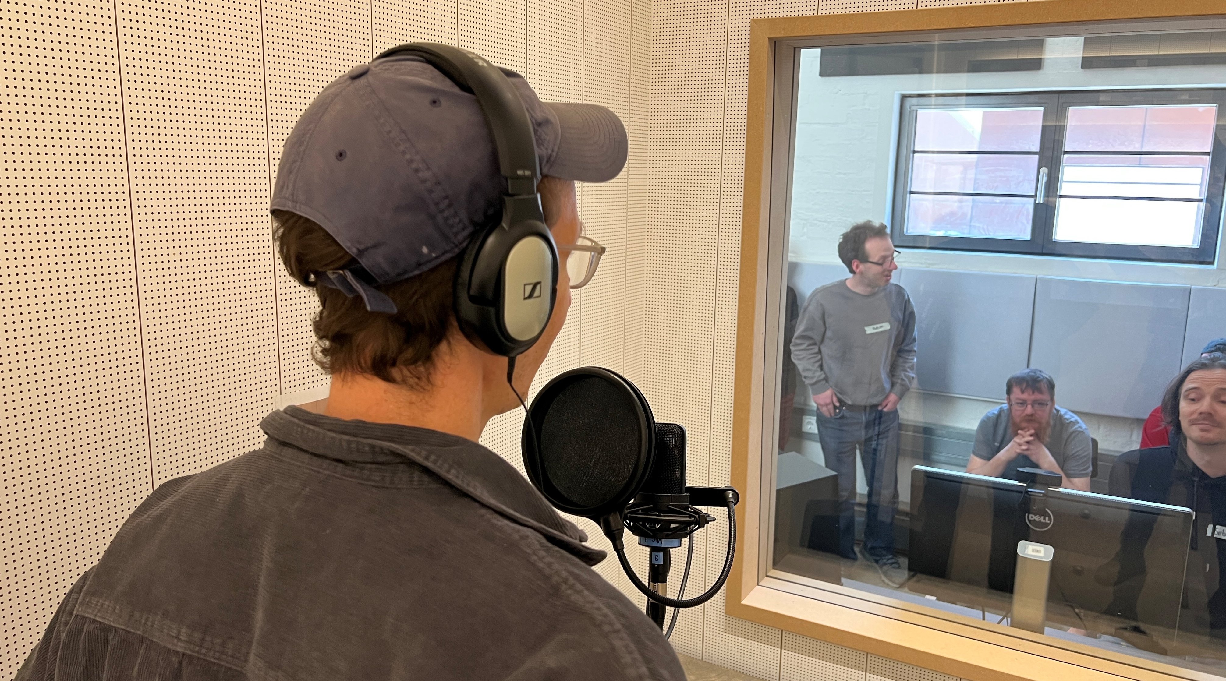 Das Foto zeigt eine Person, die sich in einem Tonstudio befindet. Die Person spricht in ein Mikrophon. 