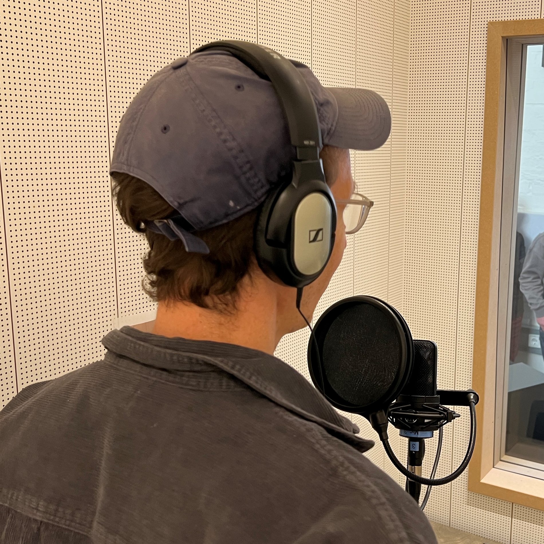 Das Foto zeigt eine Person, die sich in einem Tonstudio befindet. Die Person spricht in ein Mikrophon. 