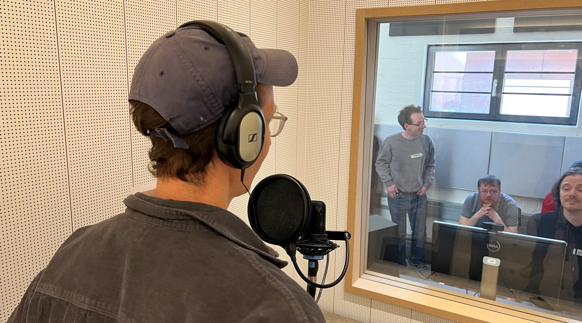 Das Foto zeigt eine Person, die sich in einem Tonstudio befindet. Die Person spricht in ein Mikrophon. 