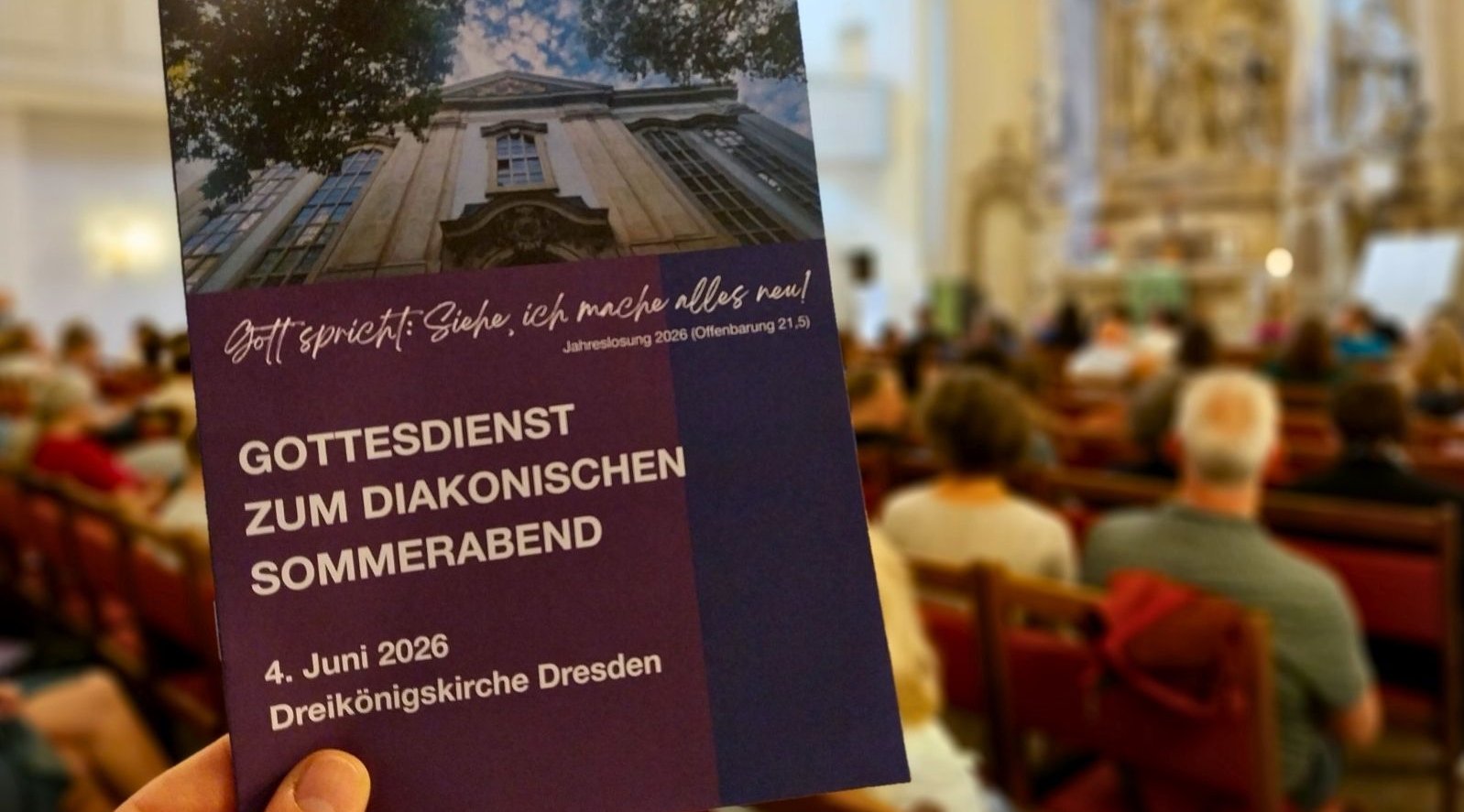 Das Bild zeigt das Liedblatt zum Gottesdienst. Im Hintergrund ist der Kirchraum mit Menschen zu erkennen. 