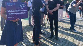 Das Bild zeigt eine Gruppe von Menschen, die sich zum Aktionstag versammelt haben. Eine Person hält ein Diakonie-Dresden-Schild in der Hand mit der Aufschrift "Nächstenliebe braucht Handlungsspielräume"
