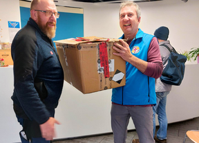 Das Bild zeigt Patrick Büttner von der Bahnhofsmission Dresden und einen Mitarbeiter der Deutschen Bahn mit einem mit gespendeter Kleidung gefüllten Karton in der Bahnhofsmission Dresden.