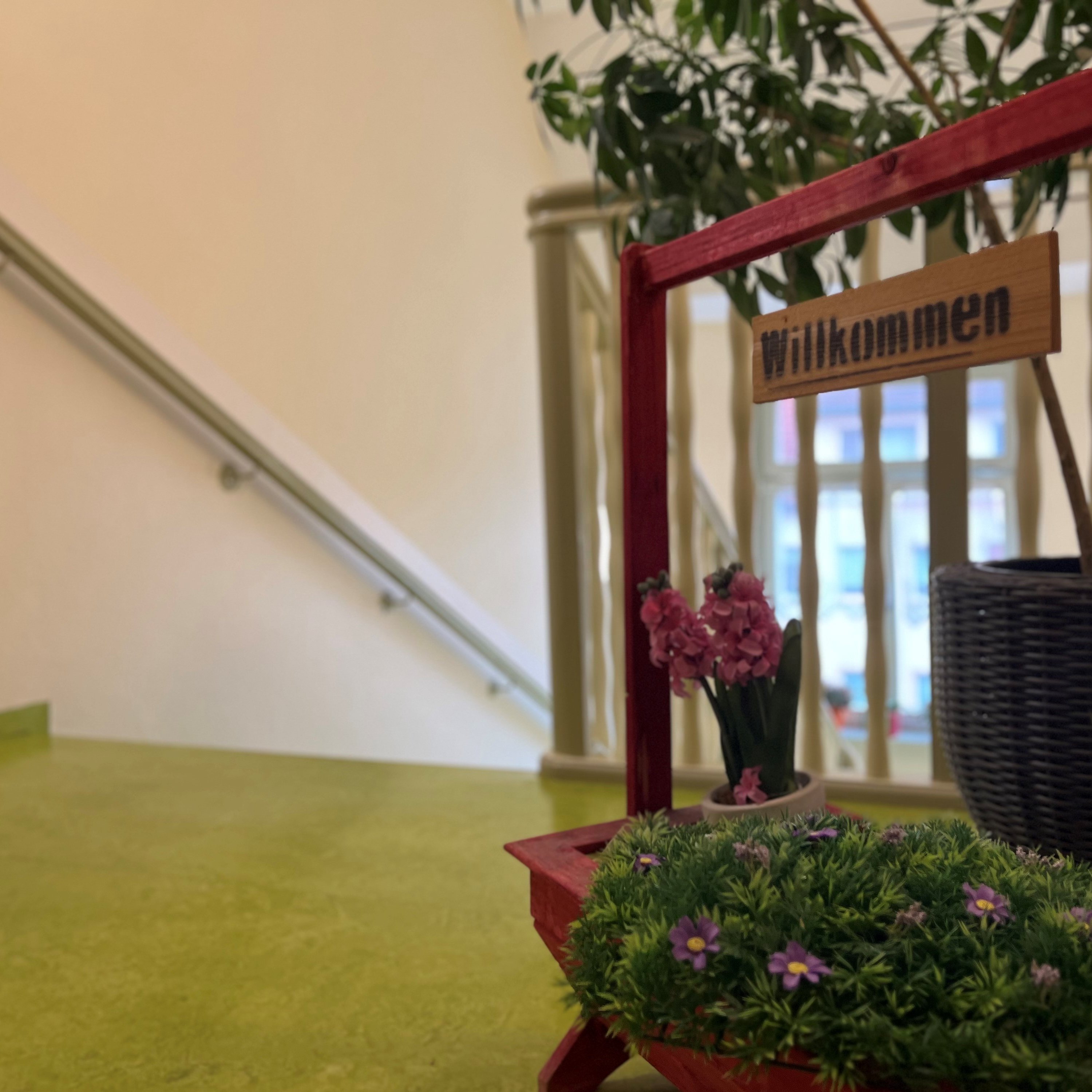 Auf dem Bild ist ein Treppenhaus zu sehen. Im Vordergrund steht ein Holzrahmen mit der Aufschrift "Willkommen".
