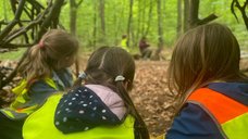 Zu sehen sind drei Kinder, die in einem Tipi aus Stöken sitzen. 