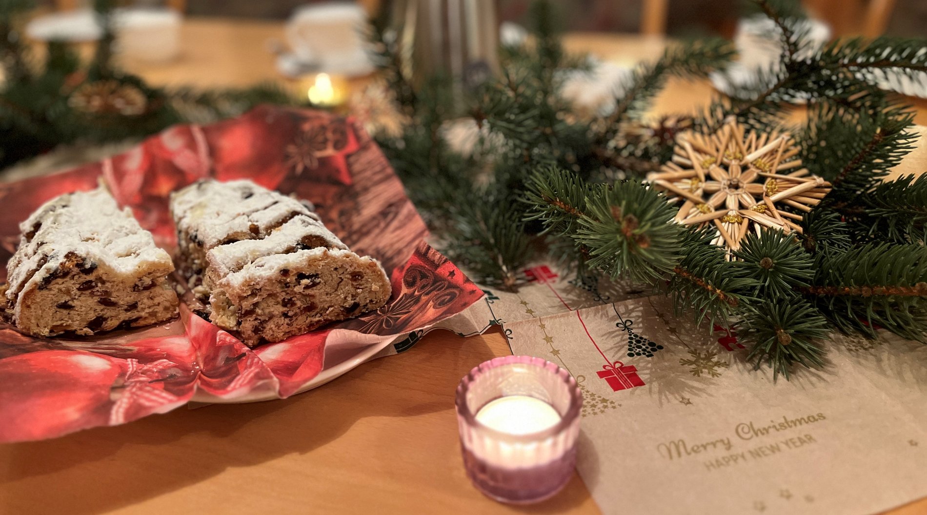 Auf einem Tisch befinden sich Tannenzweige, Stollen auf einem Teller und ein kleines Teelicht. 
