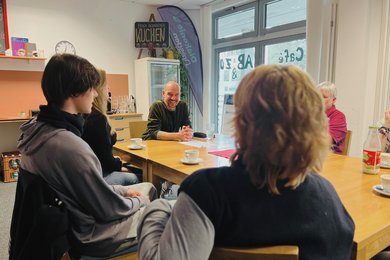 Das Bild zeigt das Café AB und Zu des ABZ. Ein Mitarbeiter befindet sich mit Schülerinnen und Schülern im Gespräch.