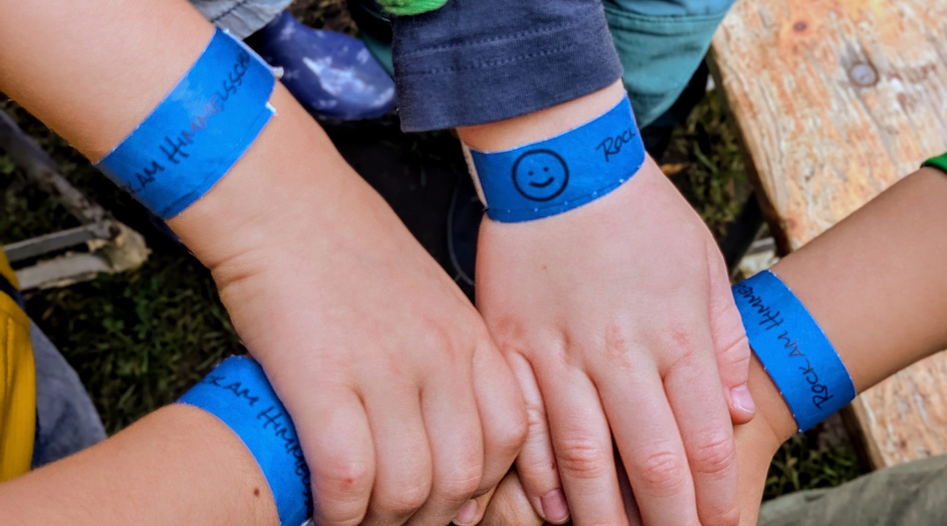 Das Bild zeigt KInderhände, die sich gegenseitig halten. Sie tragen Festivalbänder