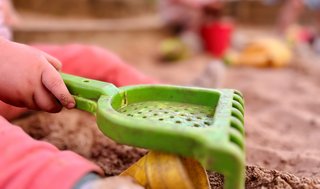 Kinderhand mit Rechen auf einem Spielplatz